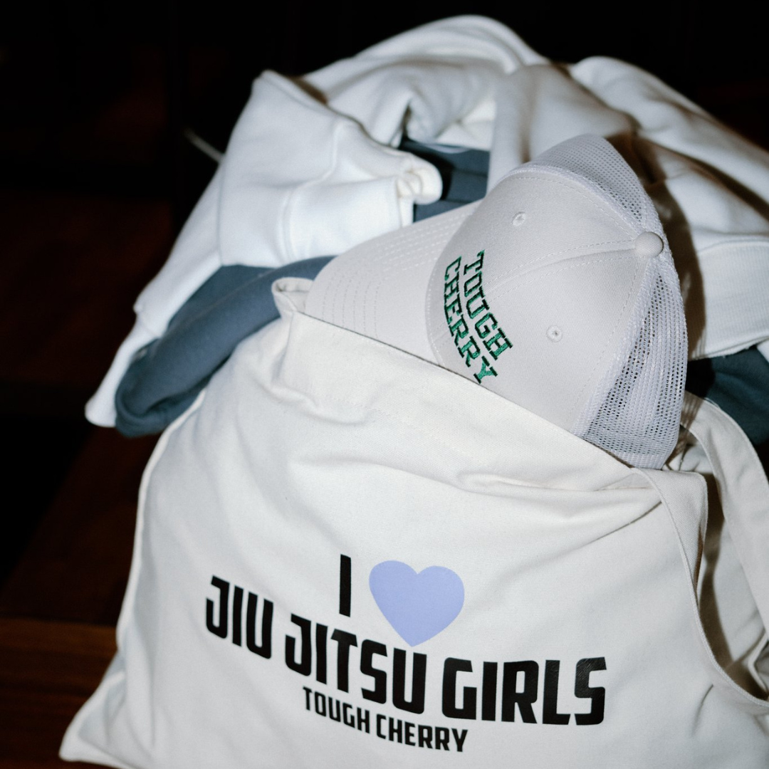 I love jiu jitsu girls tote bag filled with gym clothes and tough cherry trucker cap poking out