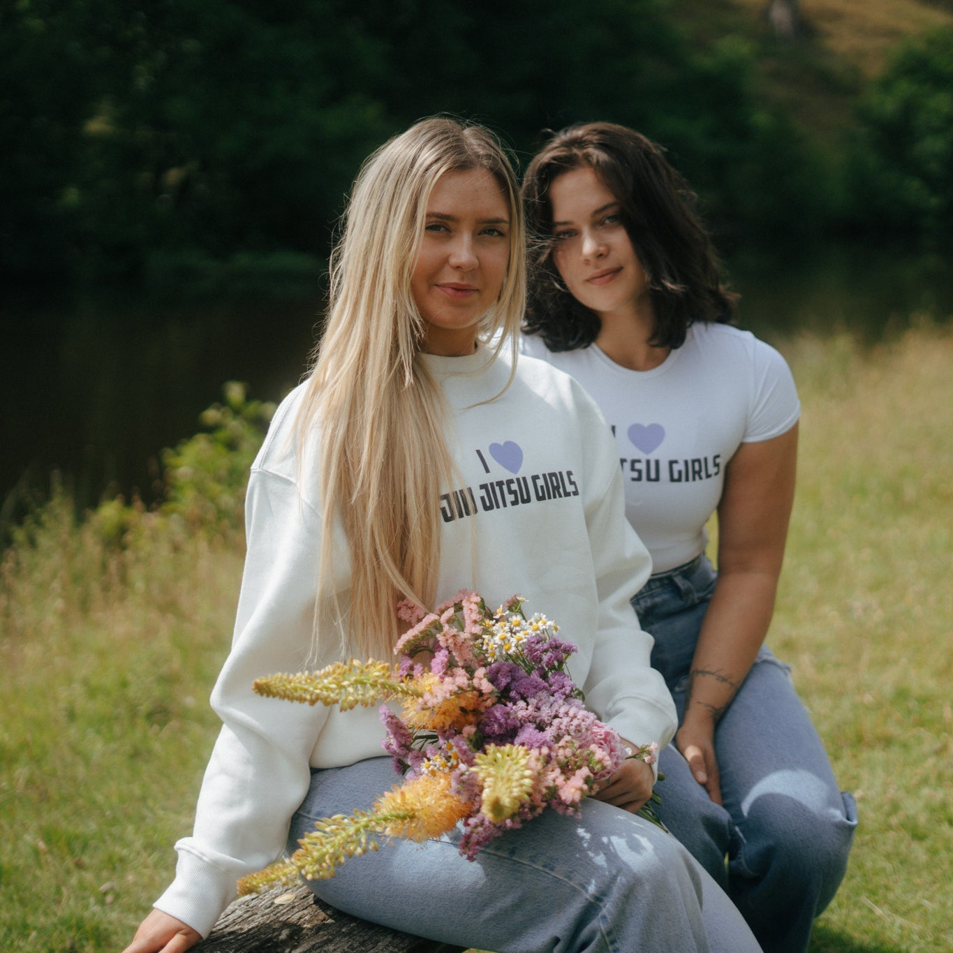 two girls in i love jiu jitsu girls tough cherry white sweatshirt and white crop top with a bouquet of flowers in a garden