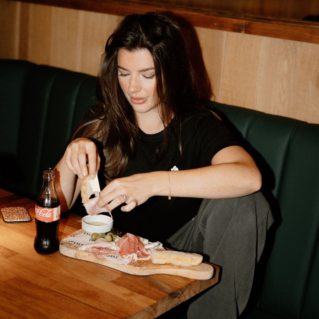 Woman sitting at a table with a charcuterie board and Coca-Cola bottle wearing tough cherry grey joggers and black rash guard.