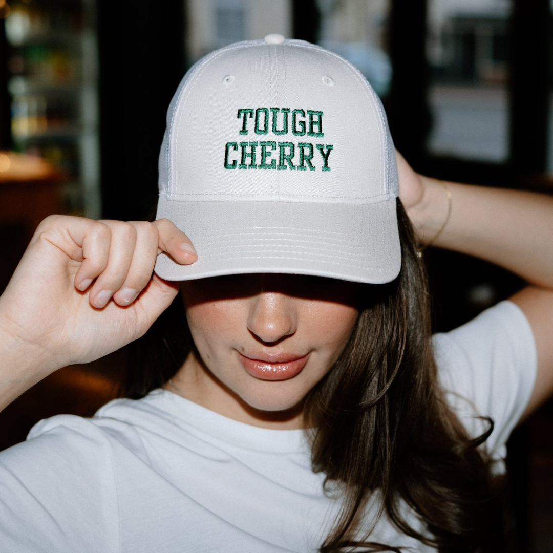 woman wearing a trucker cap with 'TOUGH CHERRY' text embroidered in a deli setting