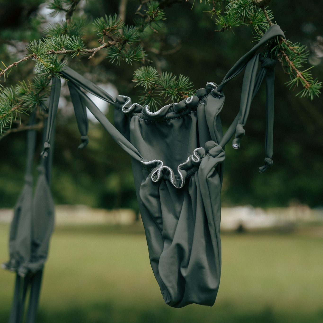 green tough cherry rushed bikini bottoms hanging from a tee branch with blurred background