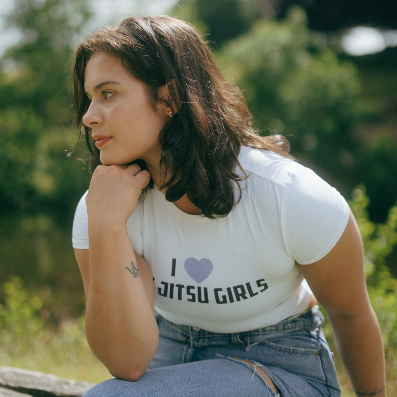Woman sitting outdoors wearing a white cropped Tough Cherry t-shirt with 'I love Jitsu Girls' text.