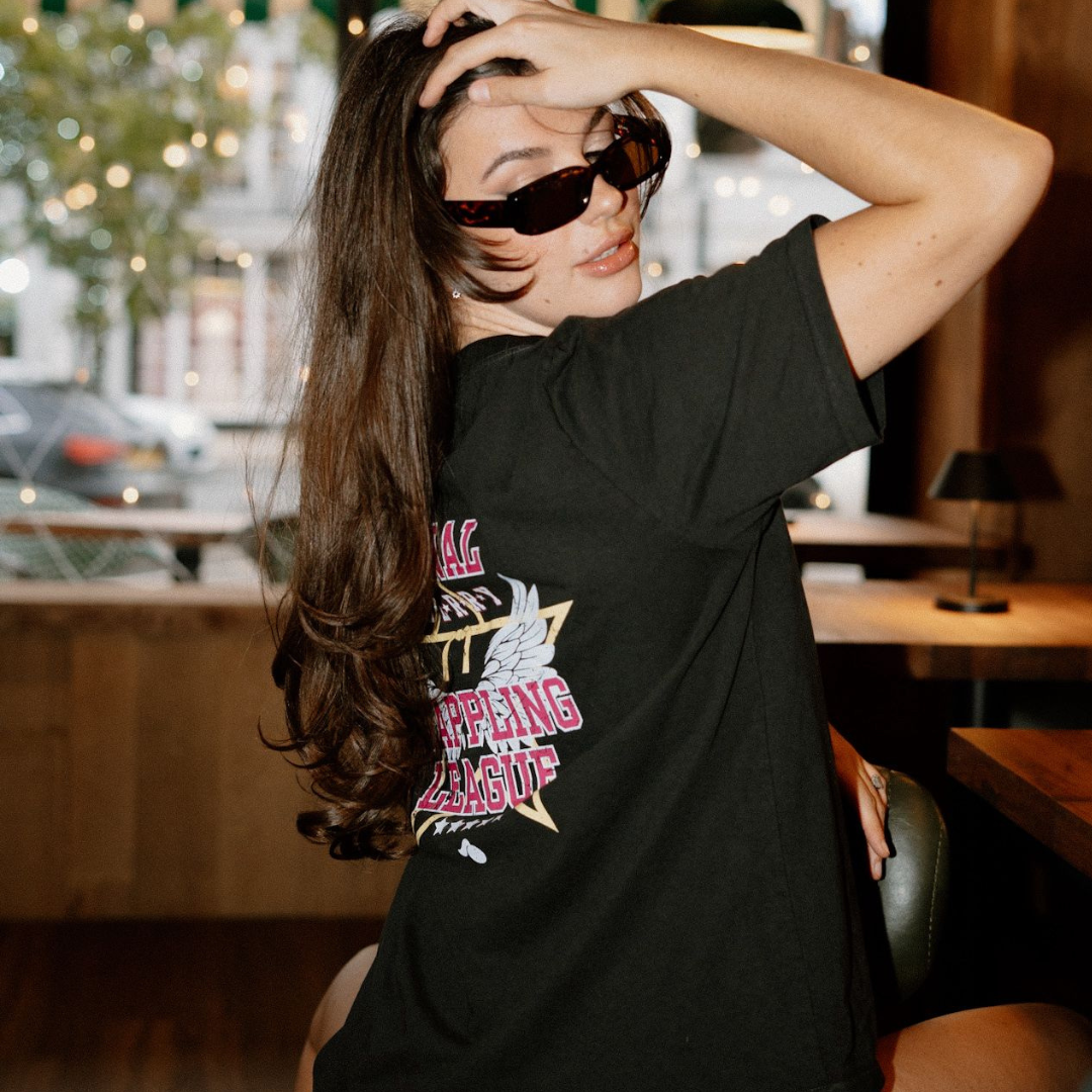 Woman wearing a black t-shirt with grappling league graphic design in an indoor setting