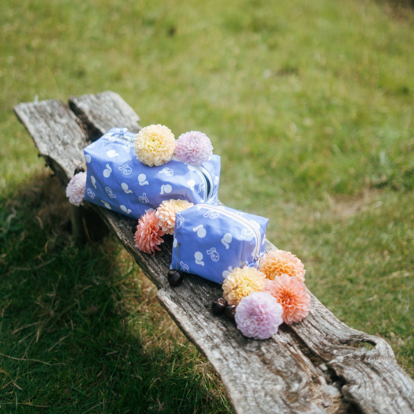 Two blue fabric tough cherry makeup bags with flowers on a wooden bench outdoors.