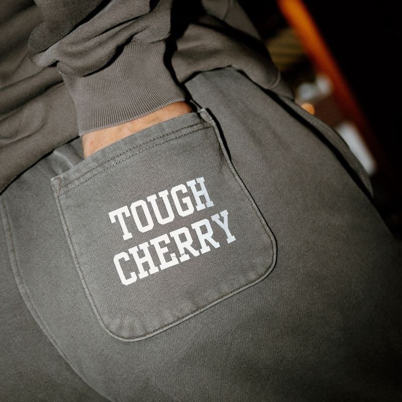 A woman wearing a white tough cherry hoodie with cherries and bows on it with a garden background. 