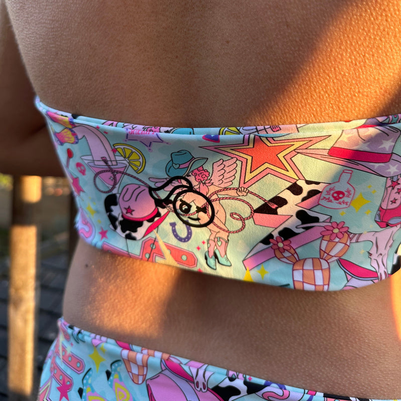 A woman's back in a tough cherry halter neck top with a black tough cherry logo showing on a disco cowgirl print.