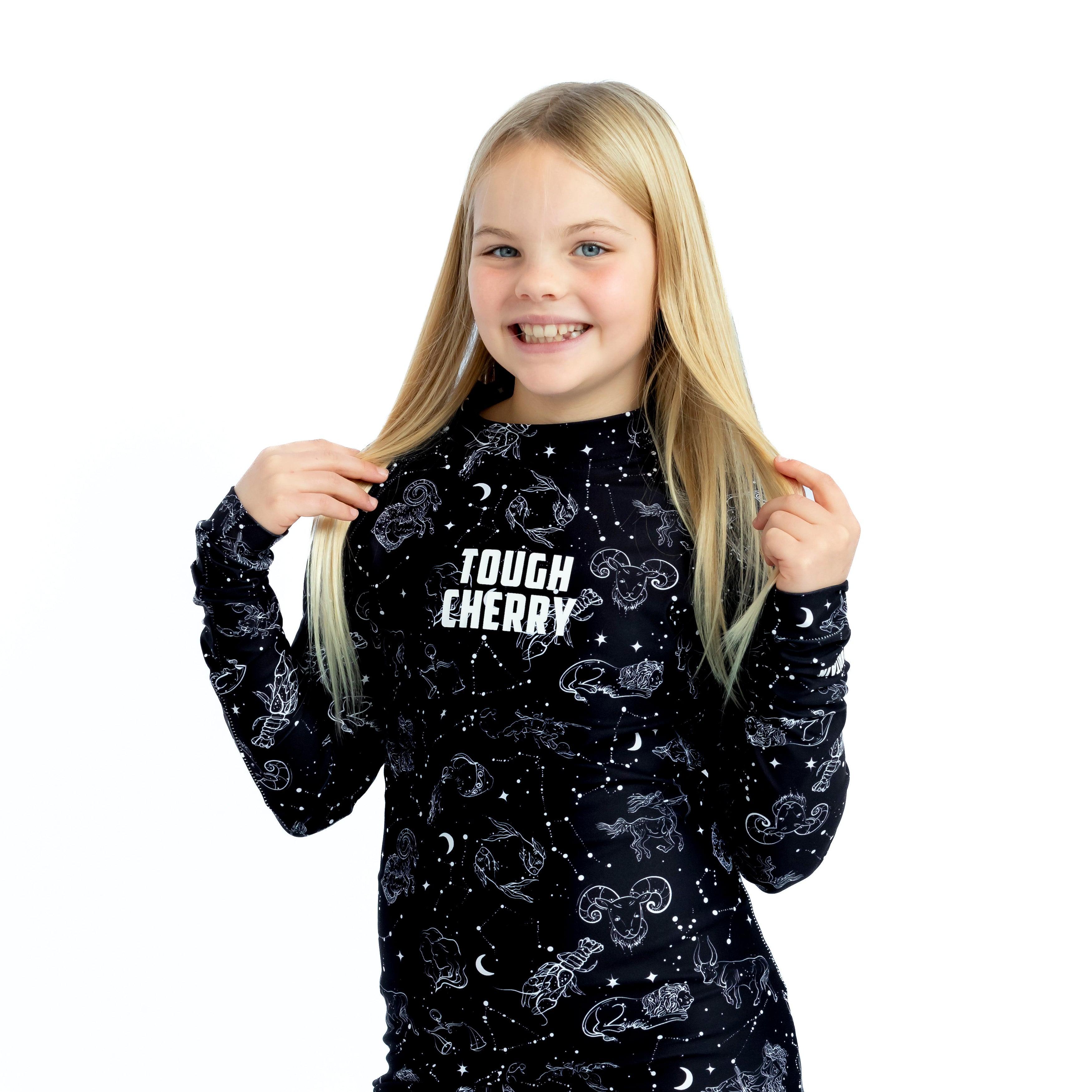 Children's under the stars long sleeved rash guard, black with white constellations print, blonde haired girl holding hair