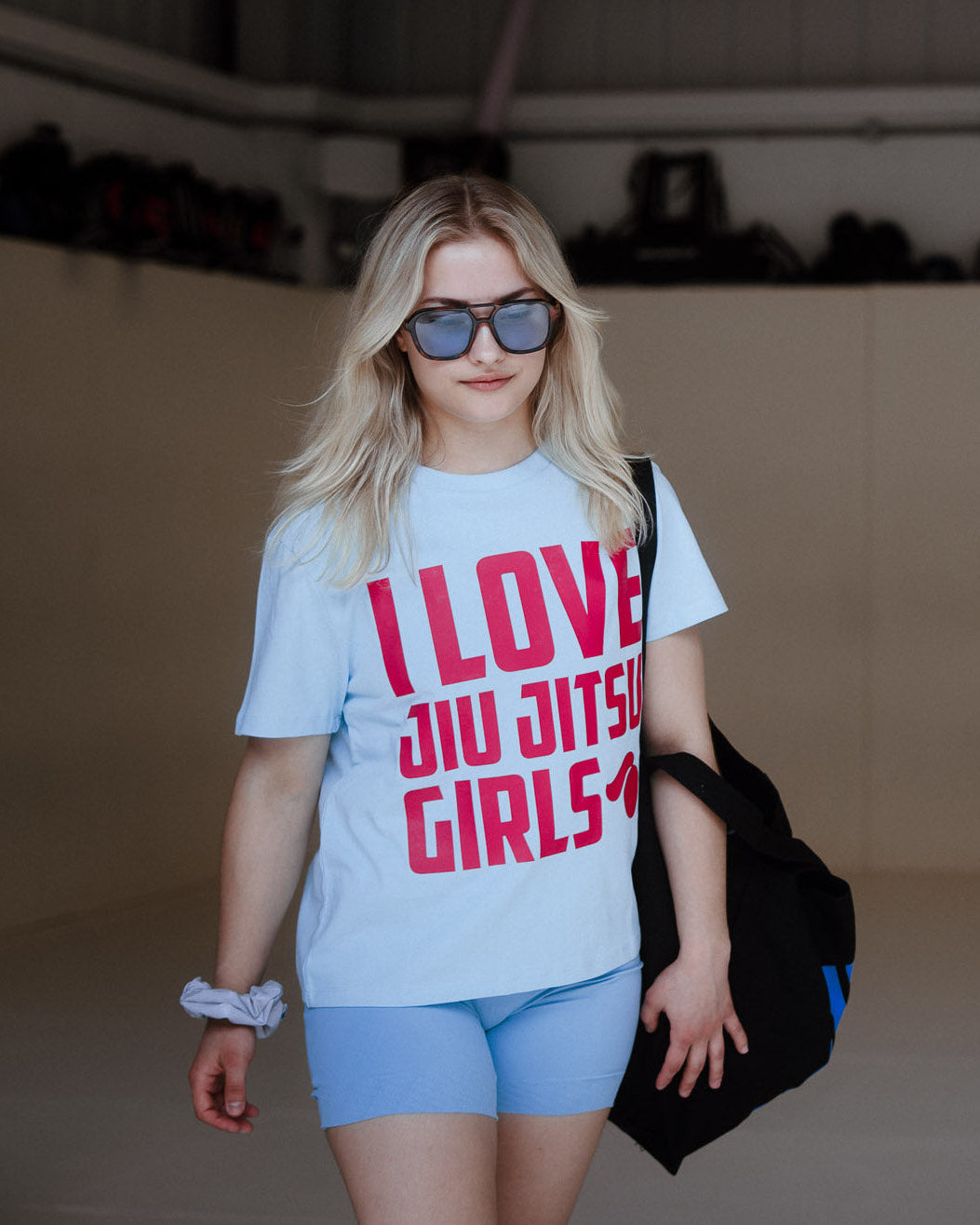 Woman wearing a t-shirt with 'I Love Jiu Jitsu Girls' text, holding a black bag.