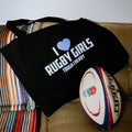 Black tote bag with 'I ❤️ Rugby Girls Tough Cherry' text on a couch next to a rugby ball.