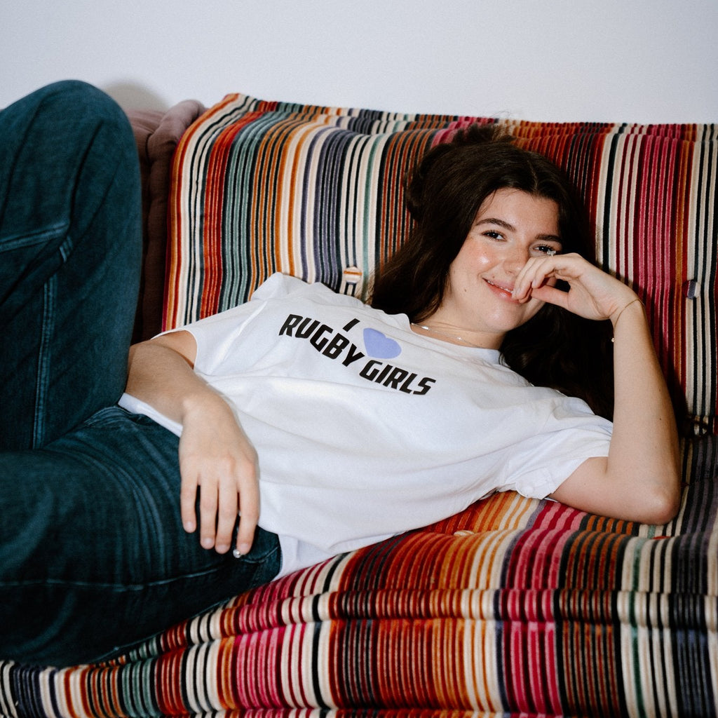 Person wearing a 'Rugby Girls' t-shirt sitting on a colorful striped couch.