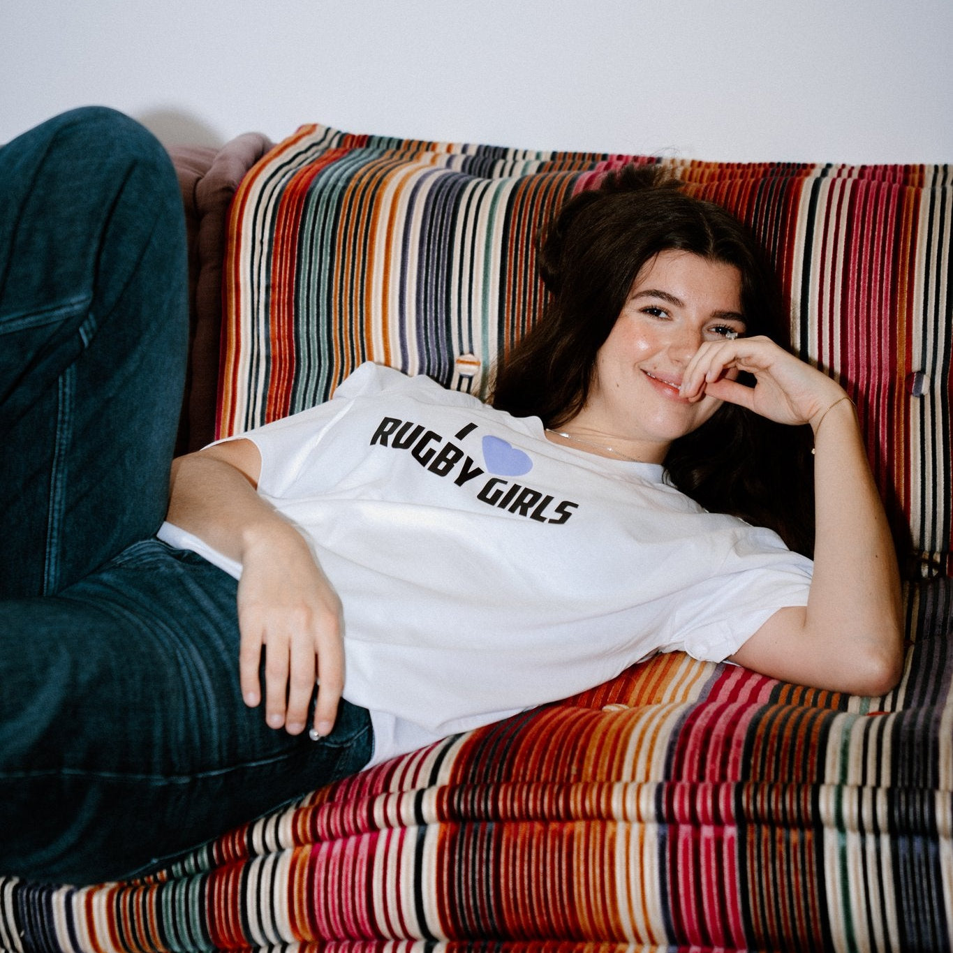Person wearing a 'Rugby Girls' t-shirt sitting on a colorful striped couch.