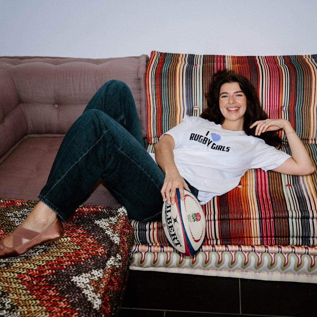 Person sitting on a colorful sofa with a rugby ball, wearing a 'Rugby Girls' t-shirt.