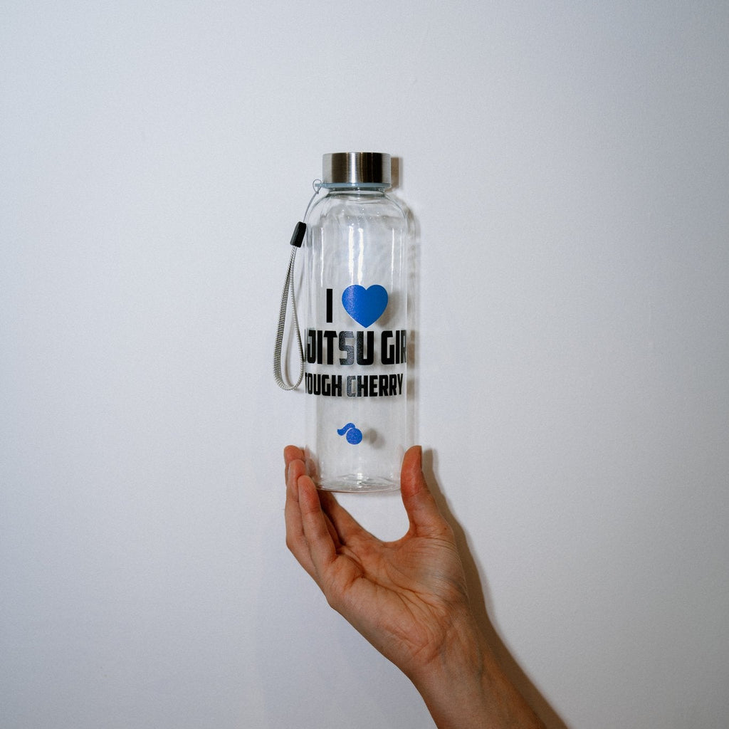Clear water bottle with text ''I love jiu jitsu girls tough cherry' and a blue heart held by a hand against a white background