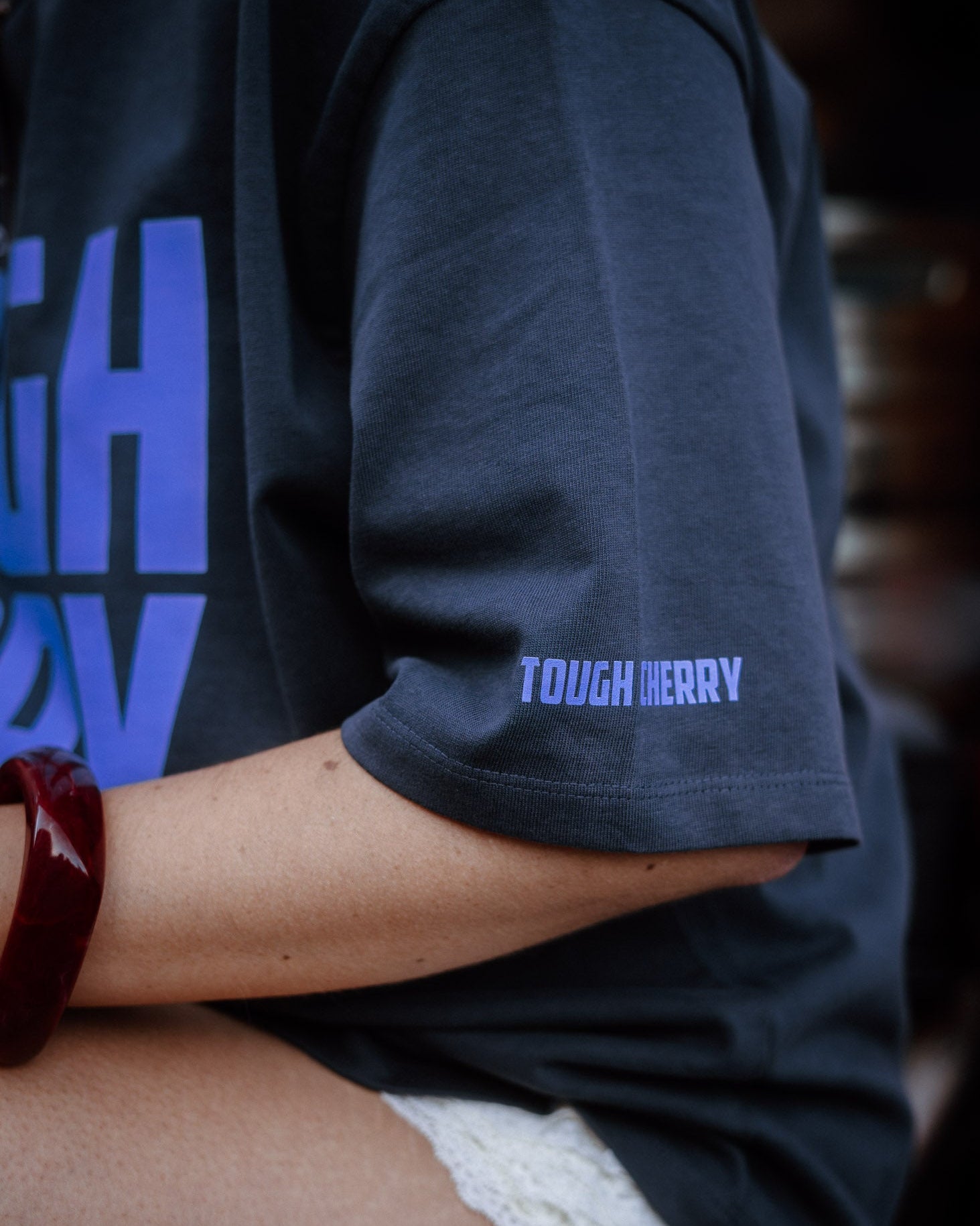 Person wearing a dark blue t-shirt with 'TOUGH CHERRY' text, blurred background