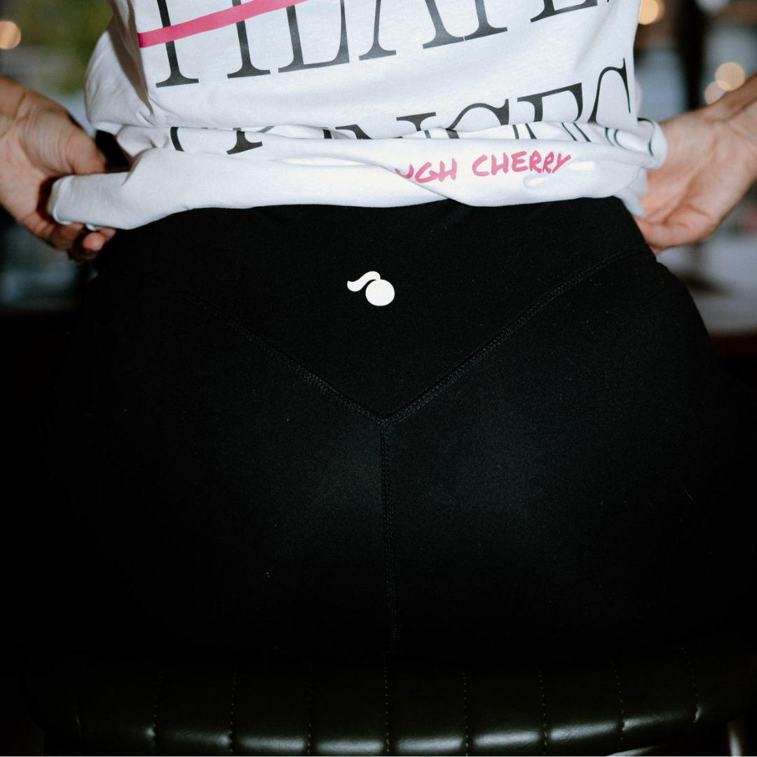 Person wearing a white t-shirt with text and black tough cherry leggings, holding the waistband.