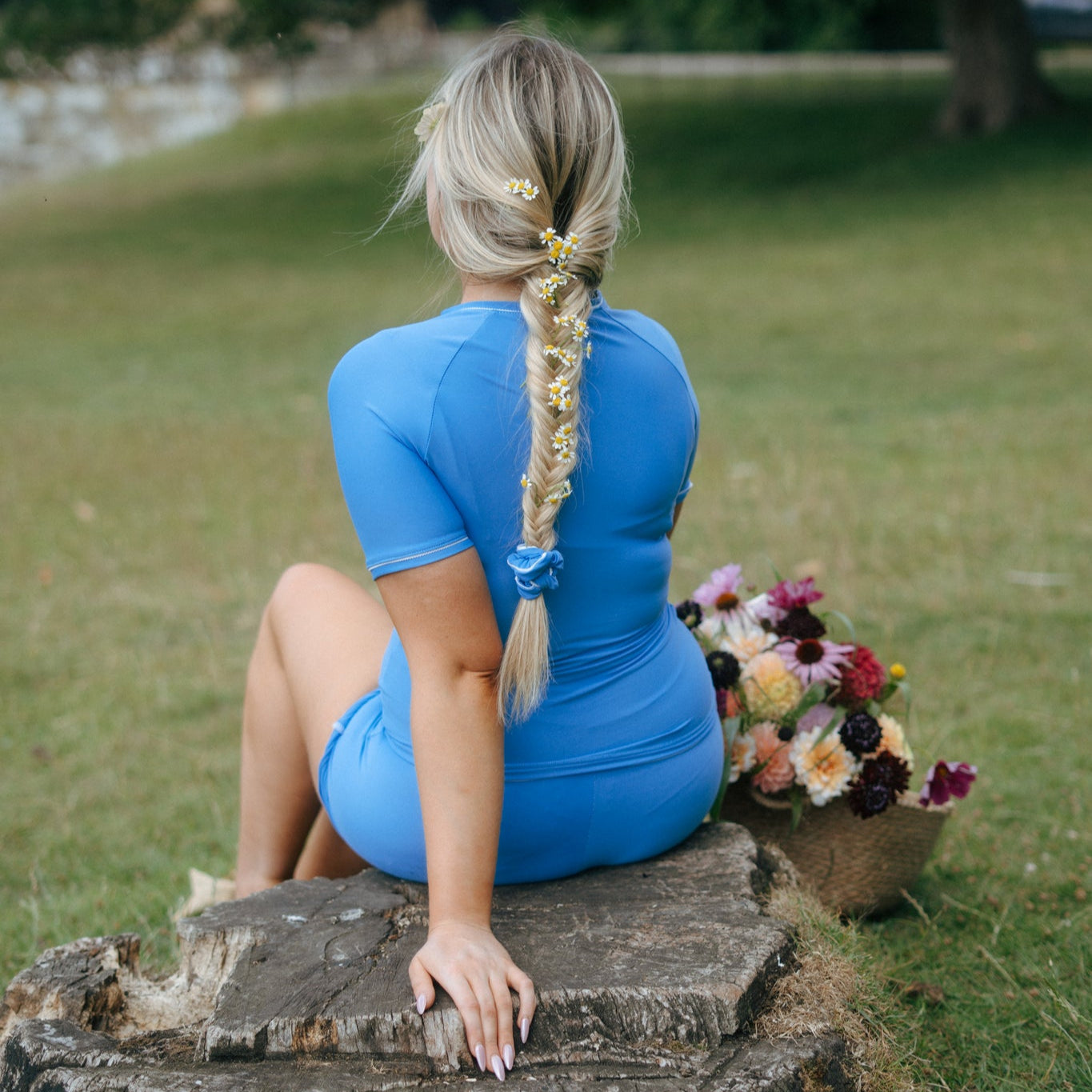 Woman in a blue tough cherry rash guard and shorts for jiu jitsu on a tree stump with flowers in a field