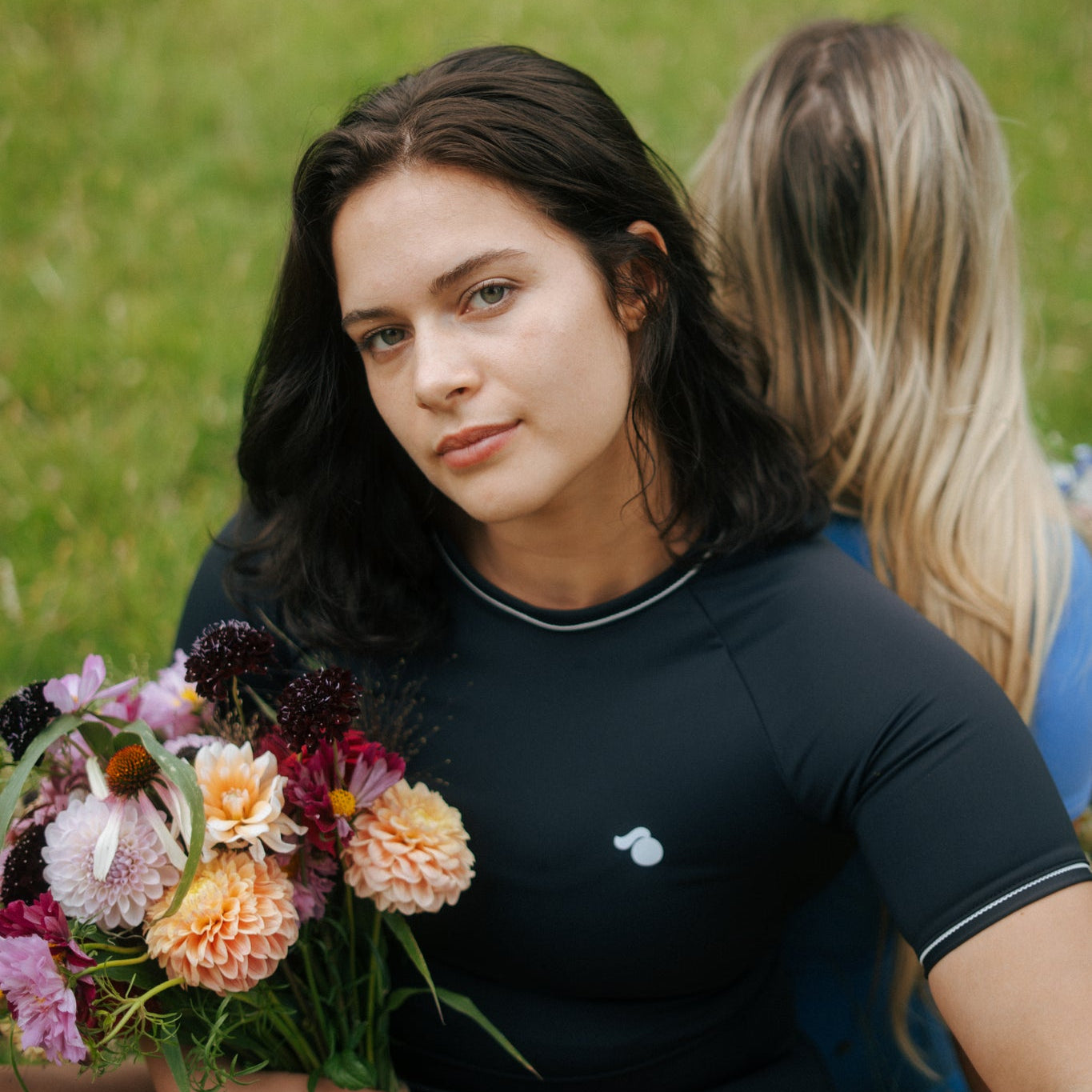 Woman holding a bouquet of flowers in a grassy field wearing a black tough cherry rash guard for jiu jitsu