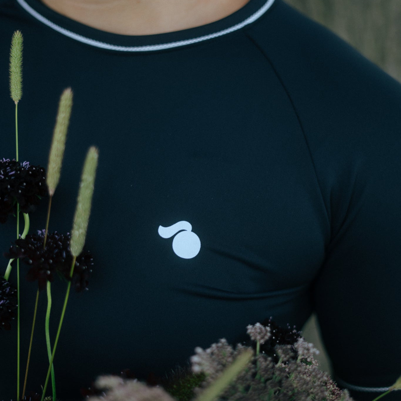 girl wearing a black tough cherry rash guard with flowers in the foreground and tough cherry face logo on the chest