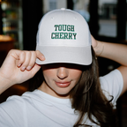 woman wearing a trucker cap with 'TOUGH CHERRY' text embroidered in a deli setting