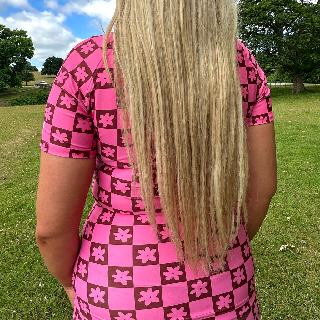 Woman wearing a Tough Cherry women's pink and Brown checkered jiu jitsu, grappling, no-gi Rash guard top with floral patterns in an outdoor setting back view. 