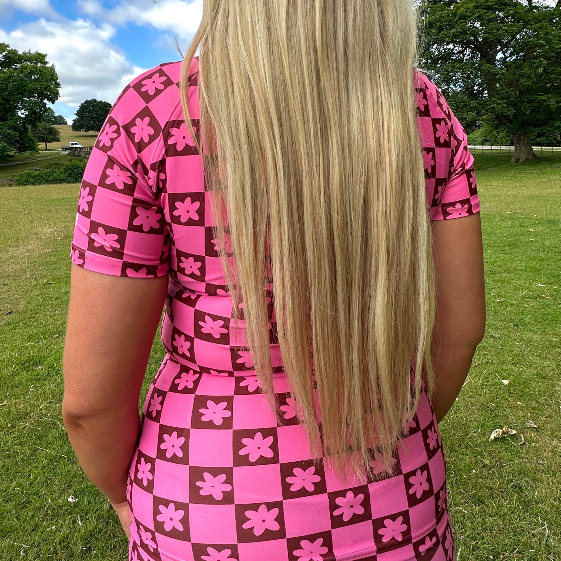 Woman wearing a Tough Cherry women's pink and Brown checkered jiu jitsu, grappling, no-gi Rash guard top with floral patterns in an outdoor setting back view. 