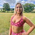 Woman wearing a Tough Cherry triangle, pink and brown checkered bikini top in an outdoor setting with trees and grass designed for surf and swim.
