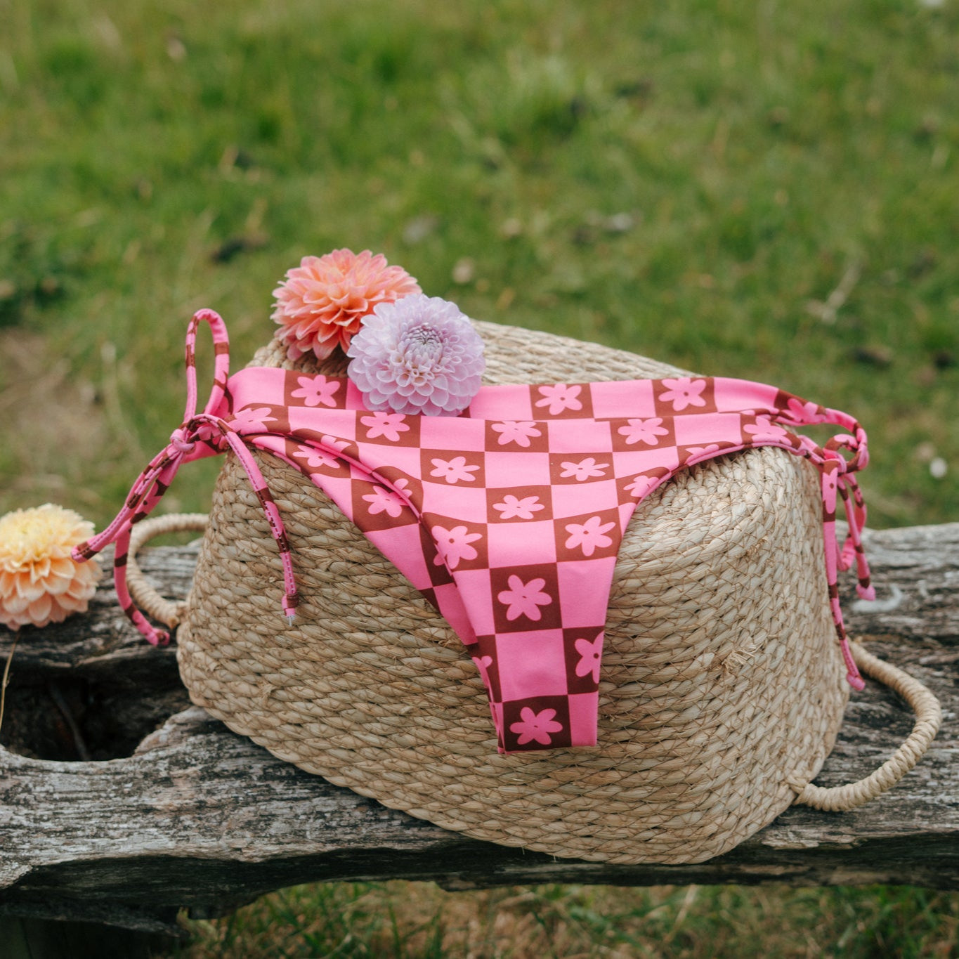 pink and brown daisy chain checkered tough cherry bikini bottoms laid on a backset in the grass