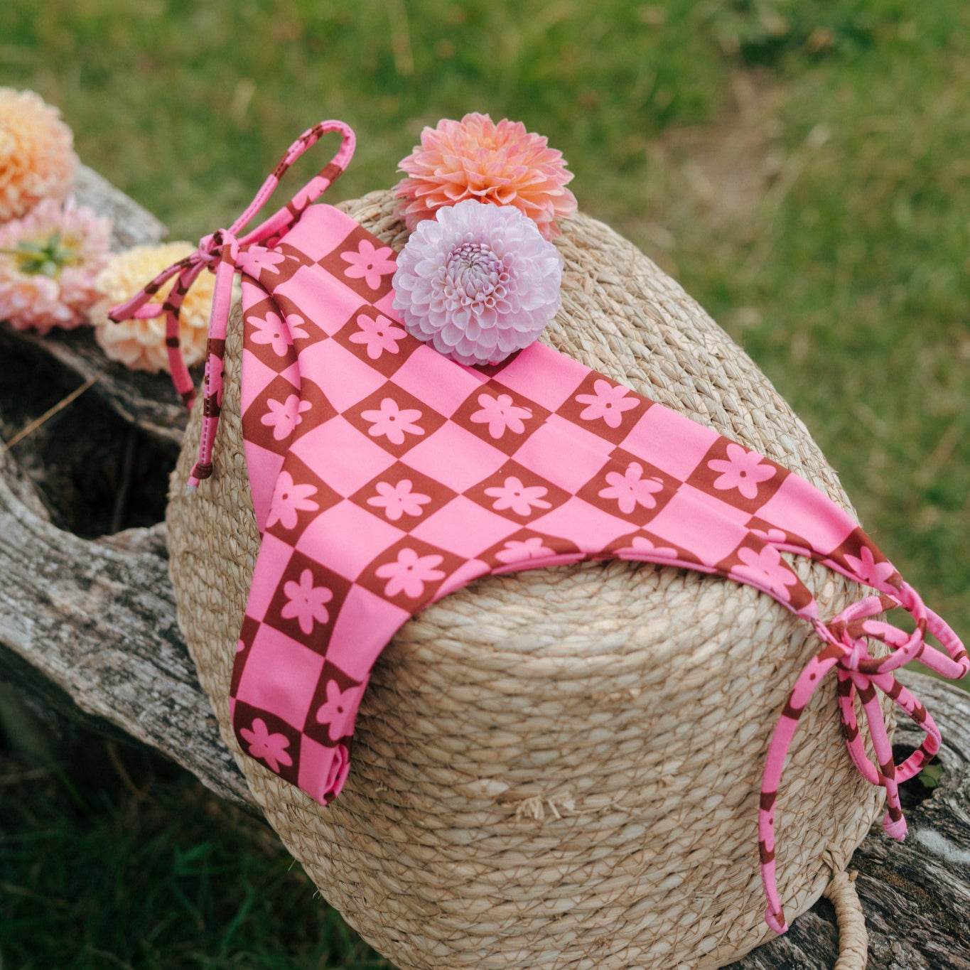 pink and brown checkered with flower print tough cherry bikini bottoms laid on a backset in the grass