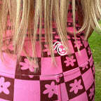 Woman wearing a Tough Cherry women's pink and Brown checkered jiu jitusu, grappling, no-gi high waisted shorts with floral patterns in an outdoor setting tough cherry logo view. 