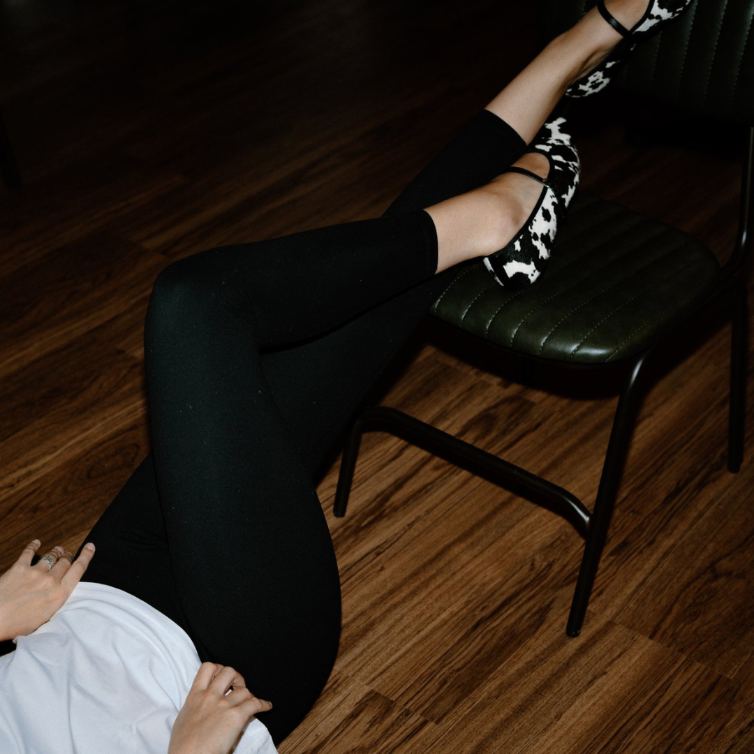 woman wearing black leggings and a patterned shoe sitting on a chair.