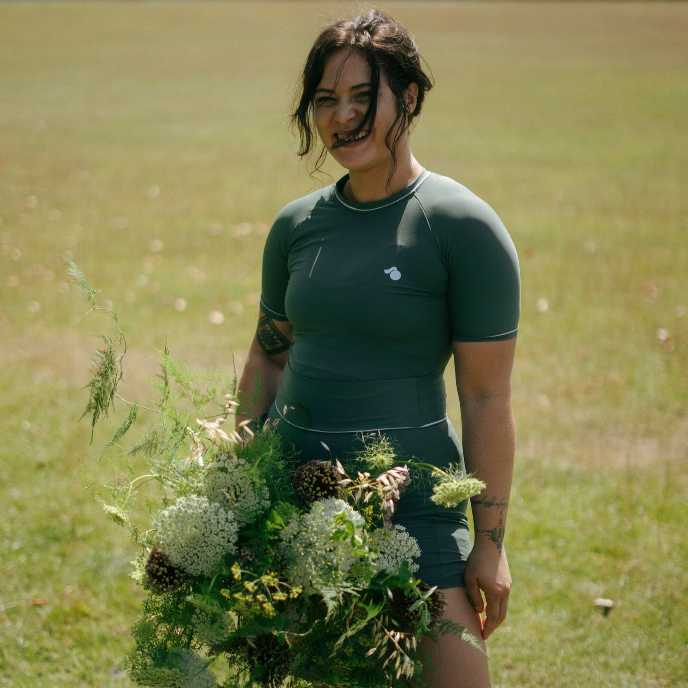 Woman holding a bouquet of flowers in a field wearing a tough cherry green rash guard and shorts for jiu jitsu