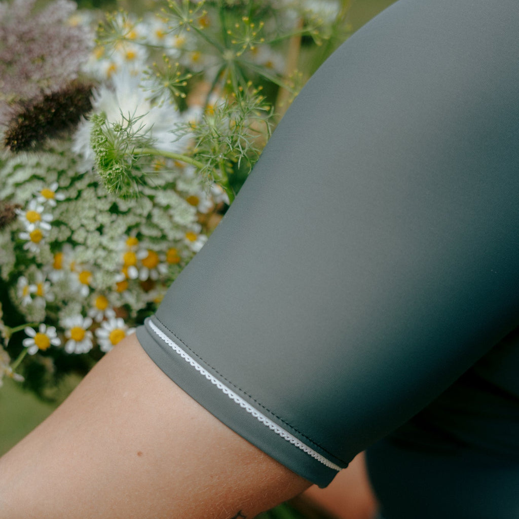 woman wearing a dark green sleeve with white trim rash guard from tough cherry, holding flowers in the background.