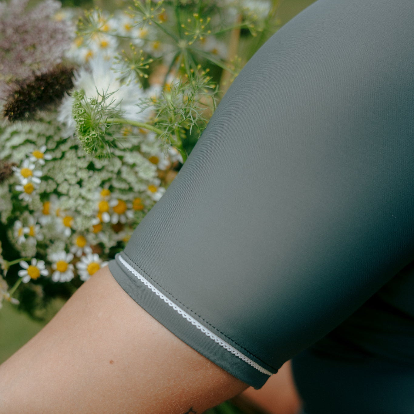 woman wearing a dark green sleeve with white trim rash guard from tough cherry, holding flowers in the background.