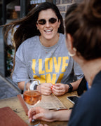 Woman wearing a 'I LOVE MMA GIRLS' shirt sitting at a table with a drink, engaged in conversation.