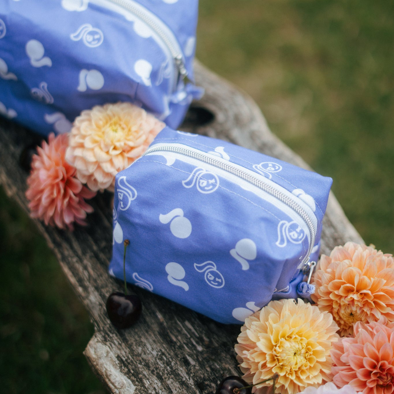 Tough Cherry blue logo makeup back with flowers around sat on a bench outdoors. 