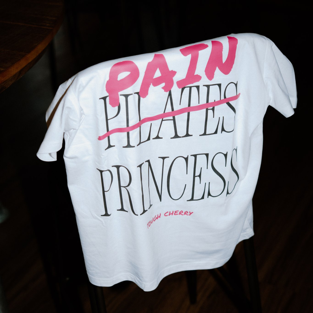 White t-shirt with pink and black text saying pain princess on a dark background