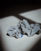 Grey reflective scrunchie with a brand label on a light surface with a dark background