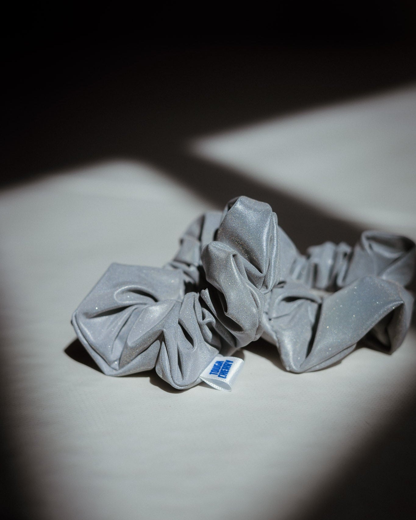 Grey reflective scrunchie with a brand label on a light surface with a dark background