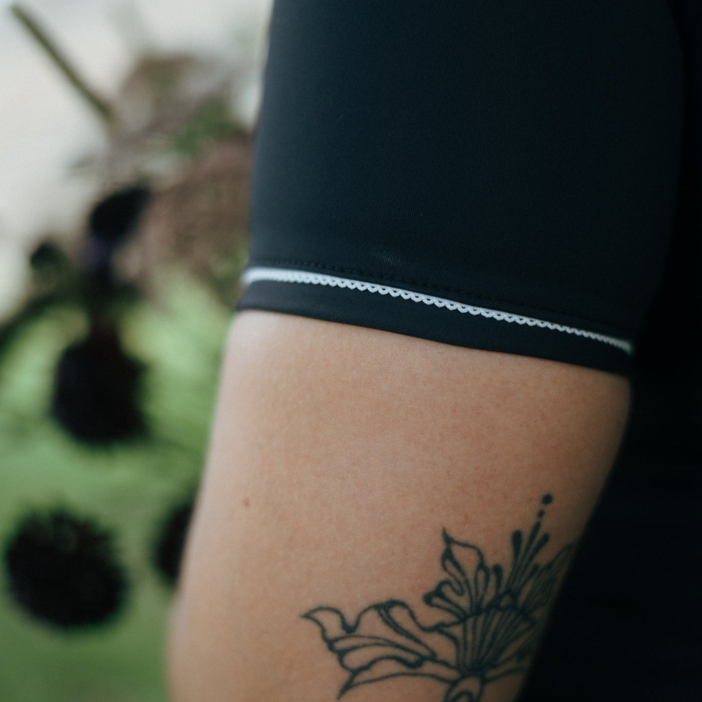 girl wearing a black sleeve tough cherry rash guard with a white trim, showing a tattoo on their arm.