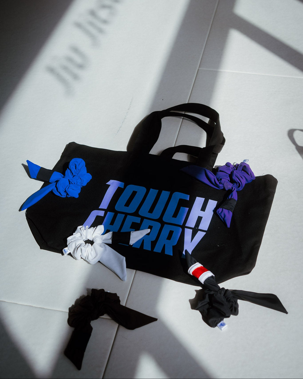 Black tote bag with 'TOUGH CHERRY' text on a light grey jiu jitsu gym floor