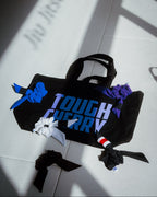 Black tote bag with 'TOUGH CHERRY' text on a light grey jiu jitsu gym floor