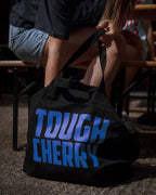 Black bag with 'TOUGH CHERRY' text on a person sitting outdoors.