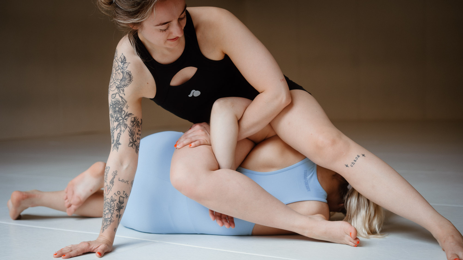 two girls wearing tough cherry one pieces in blue and black colours in a jiu jitsu gym