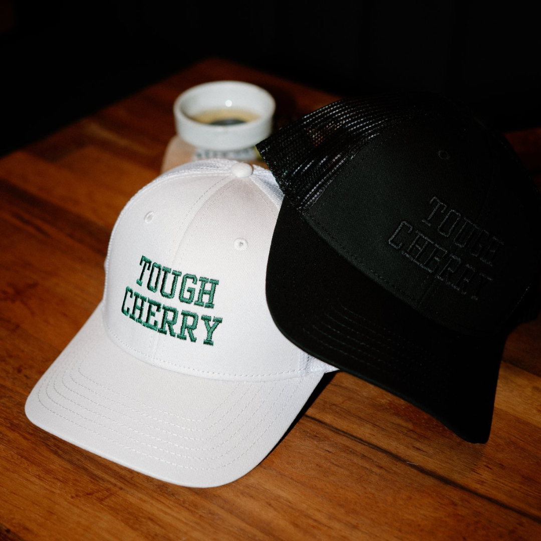 Two trucker caps with 'Tough Cherry' embroidery on a wooden surface.